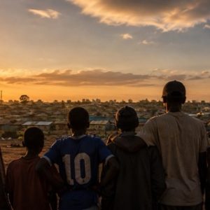 Silhouetten von Männern und Jungen, die in einer informellen Siedlung in Nairobi zusammenstehen — Sinnbild für Gemeinschaft und das Brechen des Schweigens.